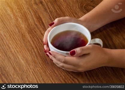 woman holding hot cup of tea on wooden table