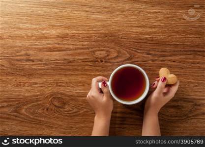 woman holding hot cup of tea with cookies on wooden table