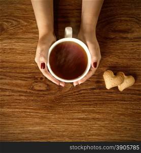 woman holding hot cup of tea with cookies on wooden table