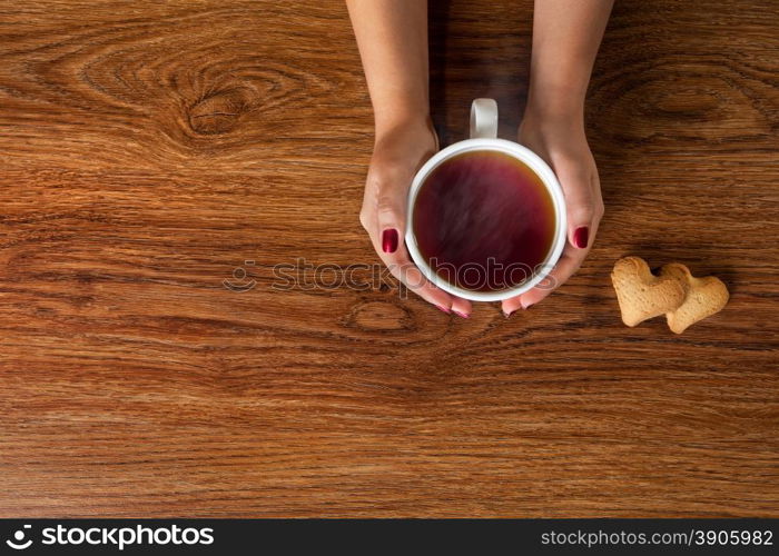 woman holding hot cup of tea with cookies on wooden table