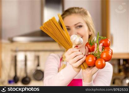 Woman holding long pasta macaron, fresh organic delicious tomatoes and garlic about to cook spaghetti.. Woman holding pasta, tomatoes and garlic