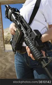 Woman holding machine gun at firing range, mid section