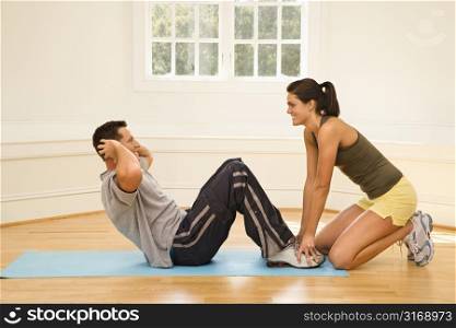 Woman holding man&acute;s feet down as he does sit up exercises.