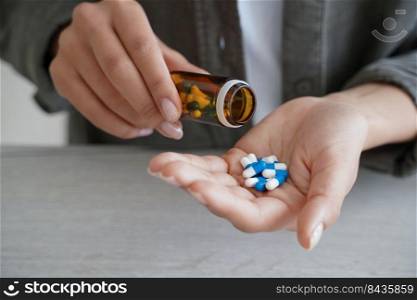 Woman holding medicine bottle pour pills into palm to take dietary supplements, vitamins or medicines, close up of female taking painkiller or sleeping tablets. Health care and wellness. Woman pour pills into palm to take dietary supplements, vitamins or medicines. Health care, wellness