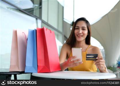 woman holding mobile smart phone & credit card for online payment with colorful shopping bags on table. consumerism lifestyle concept