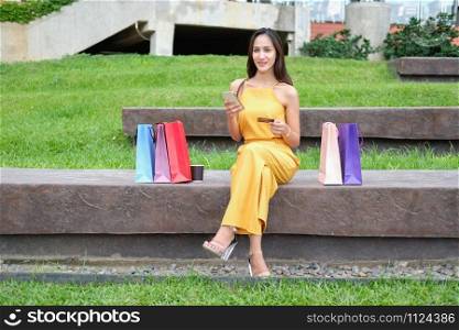 woman holding mobile smart phone & credit card for online payment with colorful shopping bags. shopaholic consumerism lifestyle concept