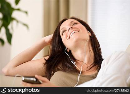 Woman holding music player listening with earbuds lying down on sofa home