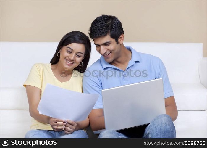 Woman holding paper while man using laptop