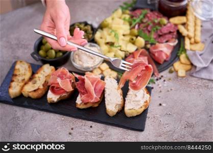Woman holding piece of prosciutto ham on a fork standing at domestic kitchen.. Woman holding piece of prosciutto ham on a fork standing at domestic kitchen