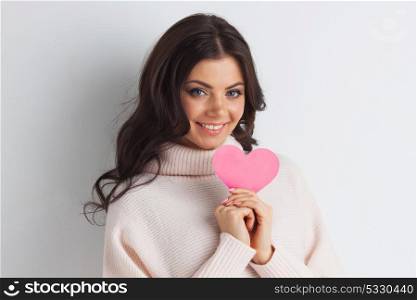 Woman holding pink paper heart. Beautiful young brunette woman holding pink paper heart, looking at camera