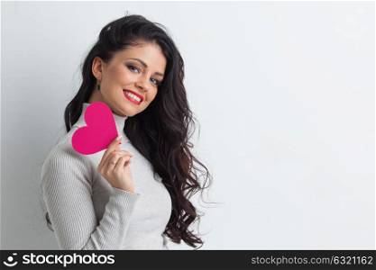 Woman holding pink paper heart. Beautiful young brunette woman holding pink paper heart, looking at camera