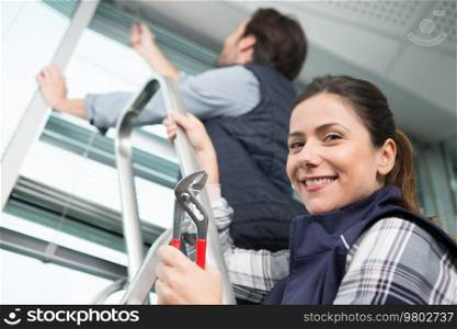 woman holding pliers while man installs window blinds