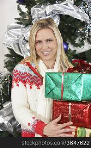 Woman holding presents in front of Christmas tree