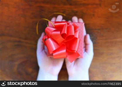 Woman holding red present box in hands for give love valentines day concept / Giving gift boxes with ribbon on wood background