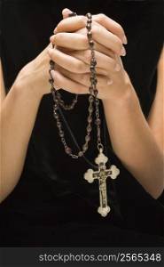 Woman holding rosary with hands clasped together.