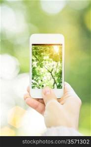 Woman holding smartphone against spring green background. Ecology concept