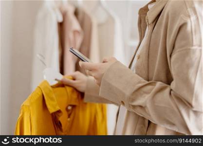 Woman holding smartphone and taking photo of her old clothes to sell them online. Selling on website, e-commerce. Reuse, second-hand concept. Conscious consumer, sustainable lifestyle. Close-up view. Woman holding smartphone and taking photo of her old clothes to sell them online. Selling on website, e-commerce. Reuse, second-hand concept. Conscious consumer, sustainable lifestyle. Close-up view.