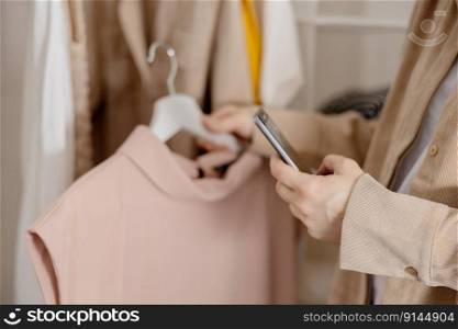 Woman holding smartphone and taking photo of her old clothes to sell them online. Selling on website, e-commerce. Reuse, second-hand concept. Conscious consumer, sustainable lifestyle. Close-up view. Woman holding smartphone and taking photo of her old clothes to sell them online. Selling on website, e-commerce. Reuse, second-hand concept. Conscious consumer, sustainable lifestyle. Close-up view.