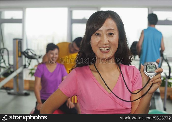 Woman holding stopwatch on foreground, people working out in the gym on the background