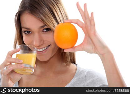 Woman holding up an orange and drinking orange juice