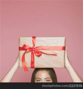 woman holding wrapped gift box her head against pink background