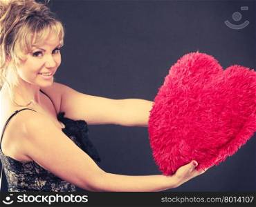 Woman holds big red heart love symbol. Woman mid age blonde female elegant evening dress holding big red heart love symbol studio shot on black. Valentines day happiness concept