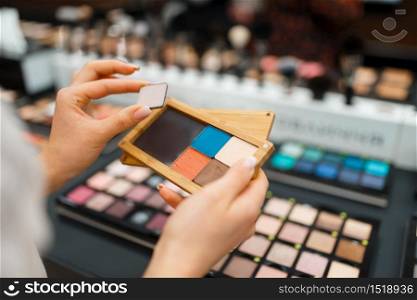 Woman holds eyeshadows at the shelf in cosmetics store. Buyer at the showcase in luxury beauty shop salon, female customer in fashion market. Woman holds eyeshadows at shelf in cosmetics store