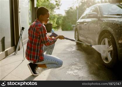 Woman holds high pressure water gun, auto wash station. Car-wash industry or business. Female person cleans her vehicle from dirt outdoors. Woman holds high pressure water gun, auto wash