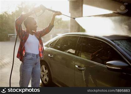 Woman holds high pressure water gun, car wash station. Carwash industry or business. Female person cleans her vehicle from dirt outdoors. Woman holds high pressure water gun, car wash