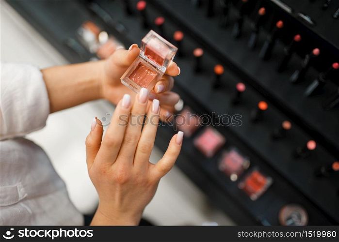 Woman holds lipstick tester in cosmetics store. Buyer at the showcase in luxury beauty shop salon, female customer in fashion market. Woman holds lipstick tester in cosmetics store