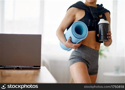 Woman holds mat, online fitness training. Female person in sportswear, internet sport workout, room interior on background. Woman holds mat, online fitness training