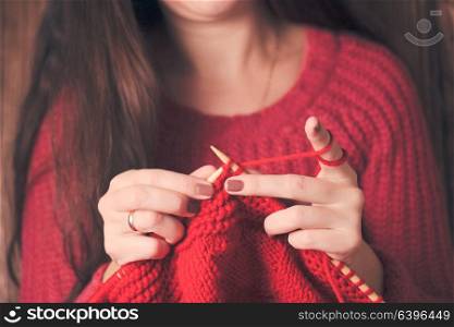 Woman holds needles and knitting a red warm jacket. Woman knits sweater