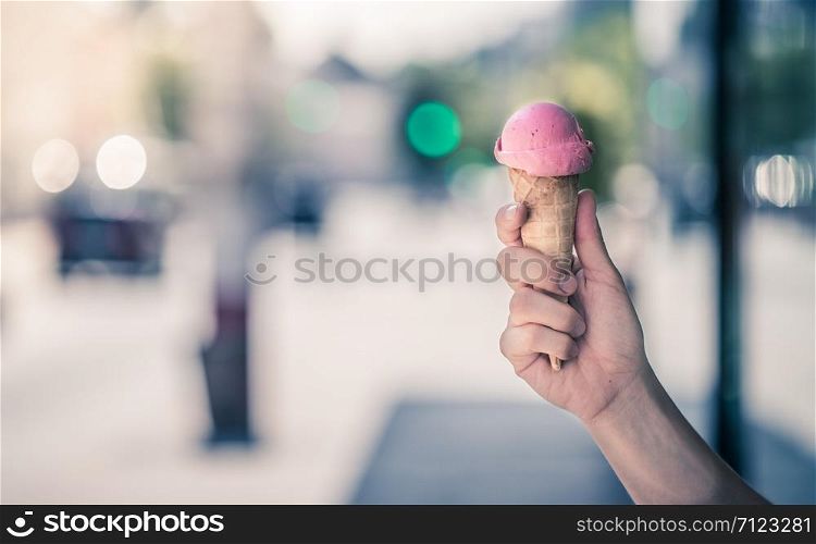 Woman holds strawberry ice cream in her hand, sunny summer day, blurry background