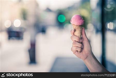 Woman holds strawberry ice cream in her hand, sunny summer day, blurry background