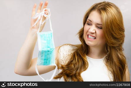 Woman holds used protective face mask, looks with disgust. Coronavirus prevention. Healthcare medical hygiene concept.. Female holds used medical face mask.