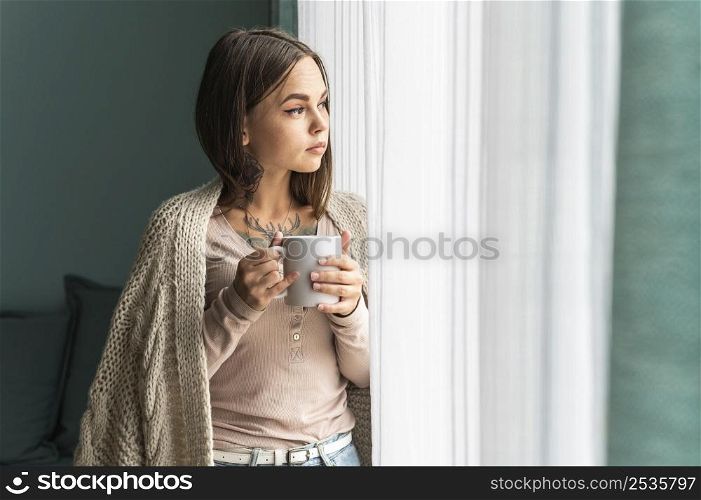 woman home having coffee looking through window during pandemic