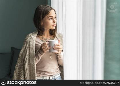 woman home having coffee looking through window during pandemic