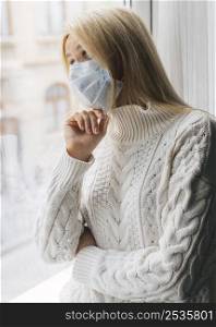 woman home with medical mask during pandemic looking through window