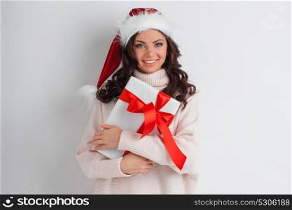 Woman hug Christmas gift. Young woman in Santa hat hug her Christmas gift