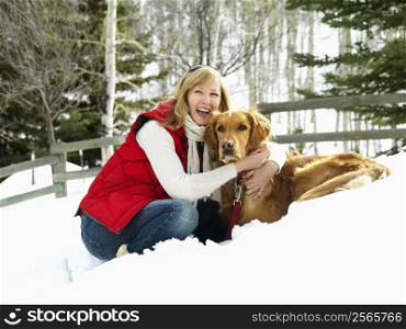 Woman hugging dog and smiling in snow covered Colorado landscape.