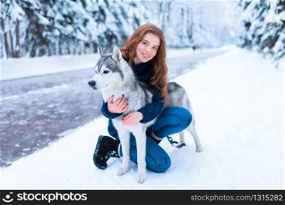 Woman hugs with siberian husky, friendship forever, snowy forest on background. Cute girl walk in park with charming dog. Woman hugs with siberian husky, friendship forever