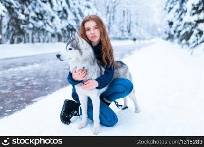 Woman hugs with siberian husky, friendship forever, snowy forest on background. Cute girl walk in park with charming dog. Woman hugs with siberian husky, friendship forever