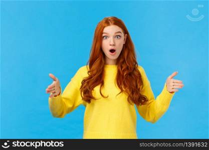 Woman impressed with enourmous size of present. Wondered and amused good-looking redhead girl in yellow winter sweater, shaping big object, showing length or distance with stretched hands.. Woman impressed with enourmous size of present. Wondered and amused good-looking redhead girl in yellow winter sweater, shaping big object, showing length or distance with stretched hands