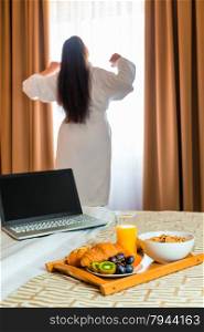 woman in a bathrobe stretches in the morning near the window