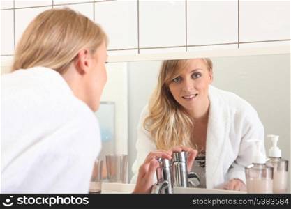 Woman in a bathroom, washing her hands in front of a mirror