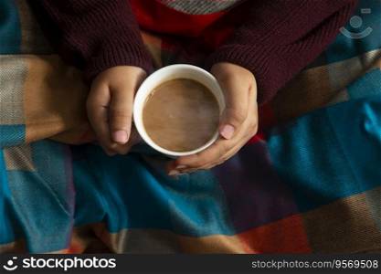 Woman in a blanket feeling the warmth of hot tea in her hand during winter