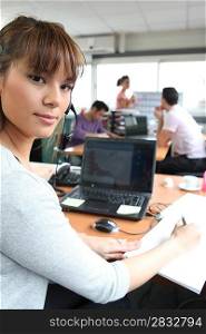 Woman in a busy office using a laptop and headset
