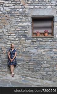 Woman in a casual clothes standing outdoors in front of an old wall near the window with flowers in pots