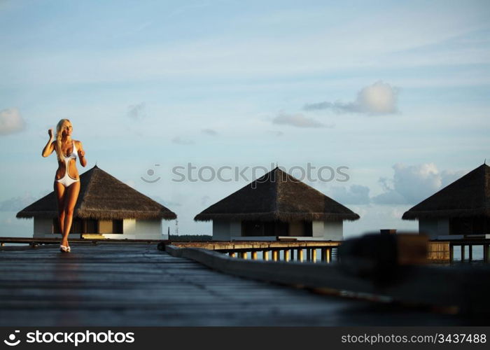 woman in a dress on a bridge home sea and the maldivian sunset on the background