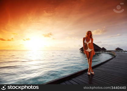 woman in a dress on a bridge home sea and the maldivian sunset on the background